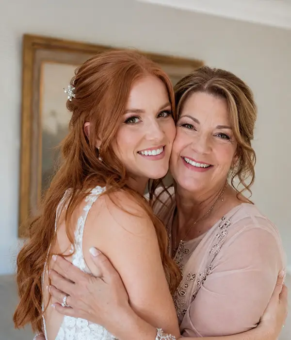 Bride and mother embracing with finished special occasion hairstyles
